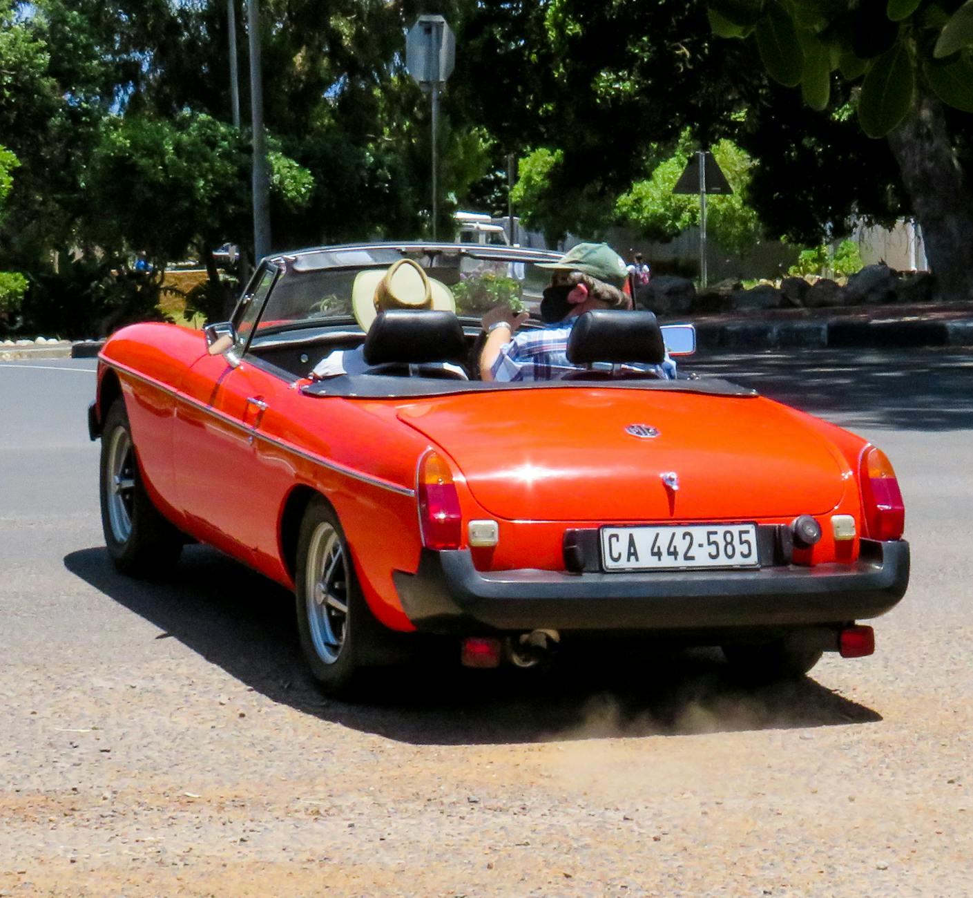 Czerwony kabriolet jedzie w słońcu, dwoje dorosłych podróżuje samochodem