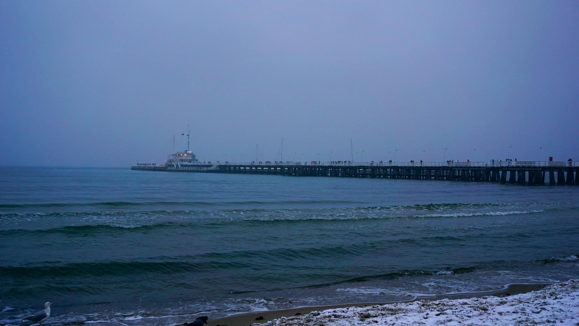 Molo w Sopocie zimą o zmierzchu, fale pod pochmurnym niebem